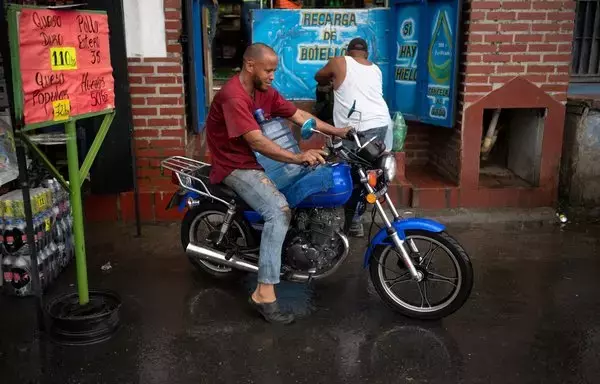 
Un hombre en motocicleta carga un bidón de agua en el barrio La Vega de Caracas. Las fallas crónicas de los servicios públicos en Venezuela provocan una 'privatización' de facto, informal y caótica, con la población obligada a cubrir con sus propios recursos el vacío dejado por la ineficacia de las redes estatales. [Federico Parra/AFP]        