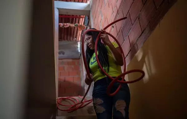 Yusmary Gómez, de 36 años, sostiene una manguera para llenar los recipientes plásticos debido a la escasez de agua, en su casa en el barrio La Vega de Caracas. Gómez ha llegado a gastar en agua la mitad del dinero que gana a la semana. Las fallas crónicas de los servicios públicos en Venezuela provocan una 'privatización' de facto, informal y caótica, con la población obligada a cubrir con sus propios recursos el vacío dejado por la ineficacia de las redes estatales. [Federico Parra/AFP]