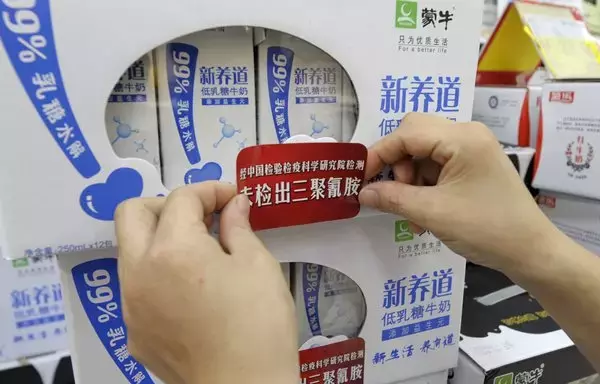 A saleswoman places a label showing the Chinese characters 'does not contain melamine' on packs of liquid milk at a supermarket in Chengdu, Sichuan province, China. The World Health Organisation warned in 2008 that at least four infants died during China's toxic milk scandal. Another 53,000 Chinese infants were sickened. [Liu Jin/AFP]