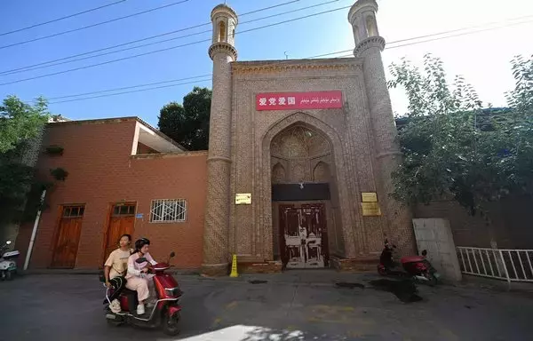 
Dos mujeres pasan en scooter por una mezquita cerrada que lleva el eslogan  "Ama al Partido Comunista, ama al país" en Kasgar, la región de Sinkiang, China, el 14 de julio. [Pedro Pardo/AFP]        