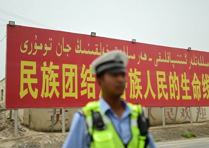 Un policía está parado frente a un cartel que dice: "La unidad nacional es el salvavidas para las personas de todos los grupos étnicos", en una carretera de la prefectura de Kasgar en la región de Sinkiang, China, el 19 de julio. [Pedro Pardo/AFP]