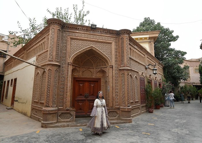 Una mujer vestida con un traje tradicional uigur posa para una fotografía en la zona turística de Kasgar Viejo en la región de Sinkiang, China, el 20 de julio. [Pedro Pardo/AFP]