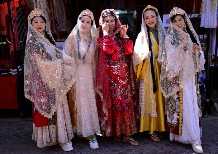 Mujeres vestidas con trajes tradicionales uigures posan para una fotografía en la zona turística de Kasgar Viejo en la región de Sinkiang, China, el 20 de julio. [Pedro Pardo/AFP]