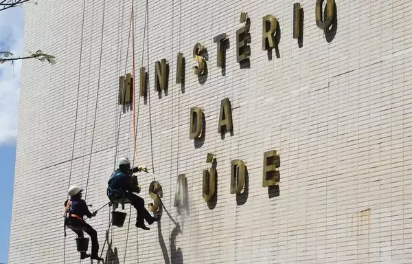 
Trabajadores limpian el frente del edificio del Ministerio de Salud en Brasil. El Ministerio de Salud de Brasil enfrenta un escrutinio por adjudicar un contrato sin licitación a una empresa ficticia asociada con una empresa farmacéutica china. [Evaristo Sa/AFP]        