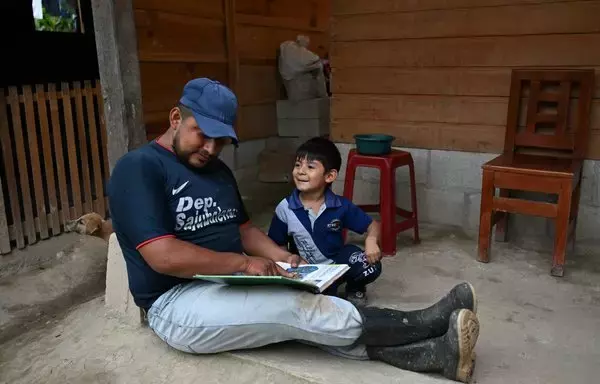 El campesino Edwin López lee un libro a su hijo Dylan, de cuatro años, en el municipio de San Juan Cotzal, Guatemala. López, como otros guatemaltecos, está apostando por ganarse la vida en su país en vez de emigrar para escapar de la pobreza. [Johan Ordoñez / AFP]