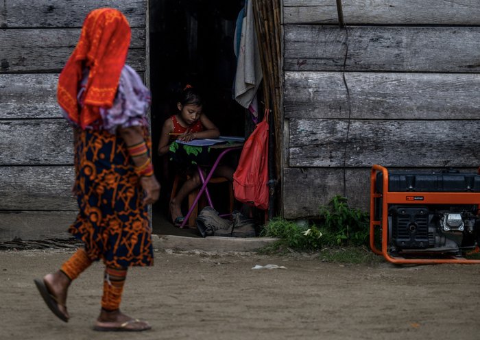 Una mujer indígena Guna pasa al lado de una niña que hace sus deberes en la isla de Carti Sugtupu. [Luis Acosta / AFP]