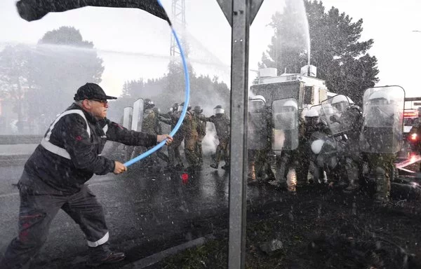 Trabajadores siderúrgicos chocan con policías antidisturbios durante una protesta contra el eventual cierre de la planta siderúrgica de Huachipato en Talcahuano, Chile. [Guillermo Salgado/AFP]