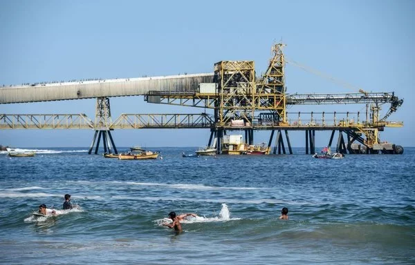 Los que disfrutan del sol se refrescan en la playa cerca del oleoducto minero de Puerto Coloso, que forma parte de la mina de cobre de Escondida, responsable de la carga y el transporte del concentrado de cobre chileno. [Martin Bernetti/AFP]