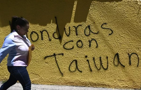 Una mujer pasa frente a un muro con un graffiti que dice "Honduras con Taiwán" en Tegucigalpa. [Orlando Sierra/AFP]