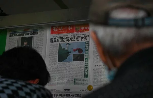 La gente lee un periódico chino con cobertura de noticias sobre los ejercicios militares de China en Taiwán, el 24 de mayo en Pekín. [Jade Gao/AFP]