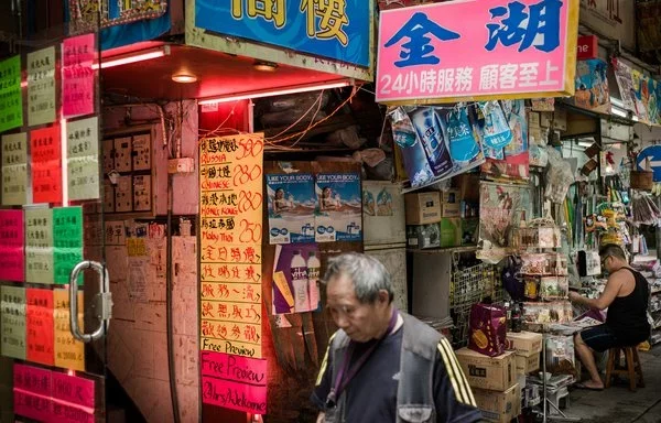 En esta foto de agosto de 2012, un peatón pasa junto a luces de neón rosas en Hong Kong que muestran los precios de las prostitutas en función de su origen étnico. [Philippe López/AFP]