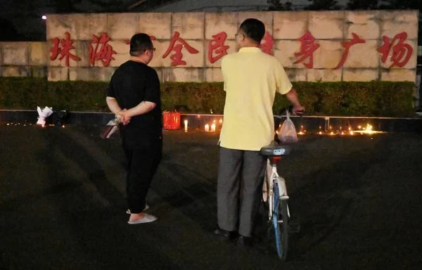 Dos hombres permanecen de pie junto a las velas dejadas en el exterior del Polideportivo de Zhuhai, un día después de que un automóvil embistiera el lugar matando a decenas de personas en la provincia china de Guangdong. [Michael Zhang/AFP]