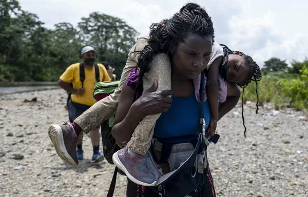 Una mujer inmigrante camina por la selva cargando a su hija cerca del pueblo de Bajo Chiquito, el primer cruce fronterizo para la provincia de Darién en Panamá. [Luis Acosta/AFP]