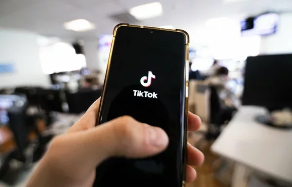 Un hombre sostiene un teléfono en el que se ve el logotipo de TikTok en una oficina de París.[Antonin Utz/AFP]