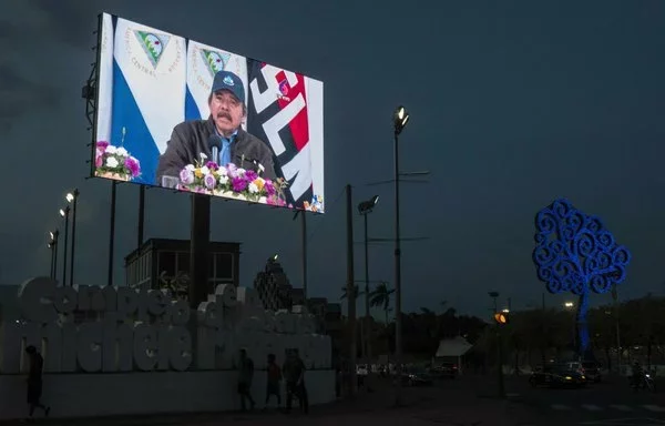 People walk in front of a screen bearing the image of President Daniel Ortega during the 125th anniversary of the birth of General Augusto C. Sandino in Managua in May 2020. [Inti Ocon/AFP]