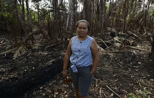 Giovana Serrao posa para una fotografía frente a sus palmeras de açaí, que fueron quemadas por un incendio descontrolado en la región amazónica del archipiélago de Marajo en Breves, Brasil. [Pablo Porciúncula/AFP]