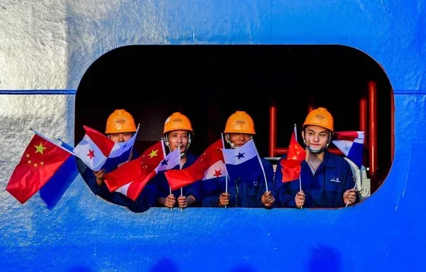 Tripulantes del portacontenedores chino Cosco Shipping Rose ondean las banderas china y panameña a su paso por las Esclusas de Cocolí, en el Canal de Panamá. [Luis Acosta/AFP]